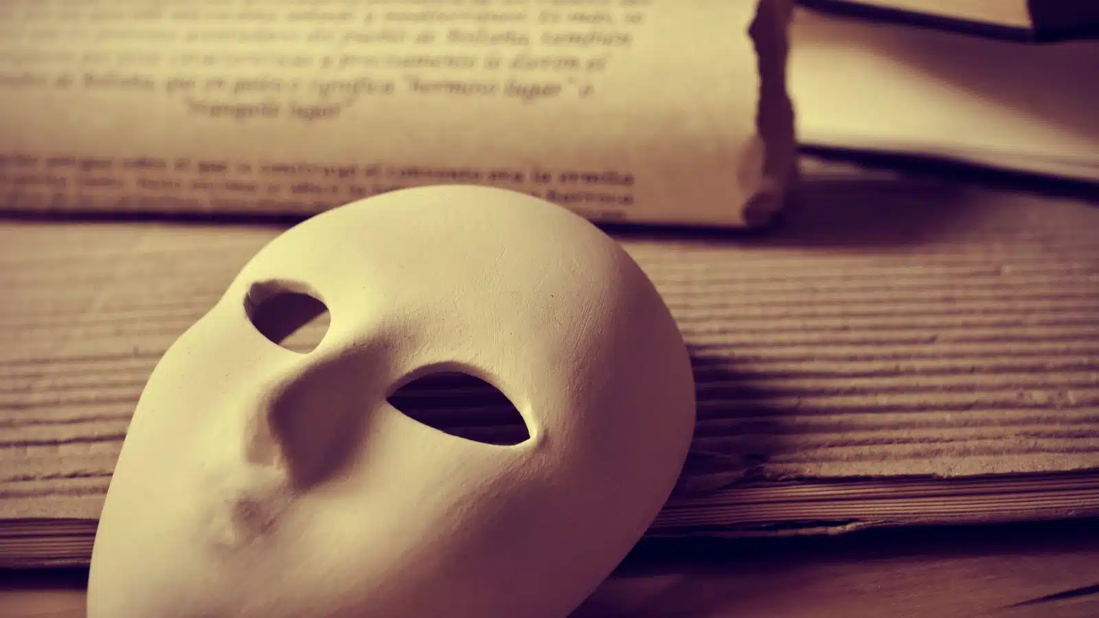 A blank drama mask laying on typed pages to represent how to build suspense during your rising action sequence.