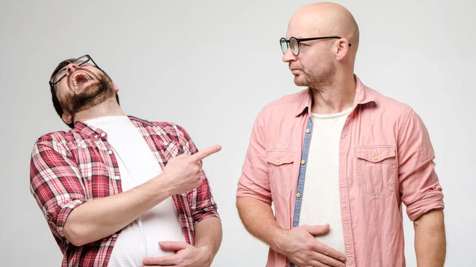 An obnoxious man laughs loudly while another man stares at him for the off-putting behavior. 