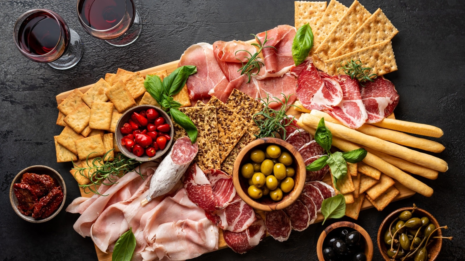 A tray featuring crackers, meats, cheese, and olives to represent party snacks.