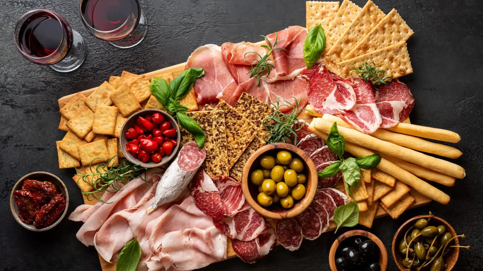 A tray featuring crackers, meats, cheese, and olives to represent party snacks.