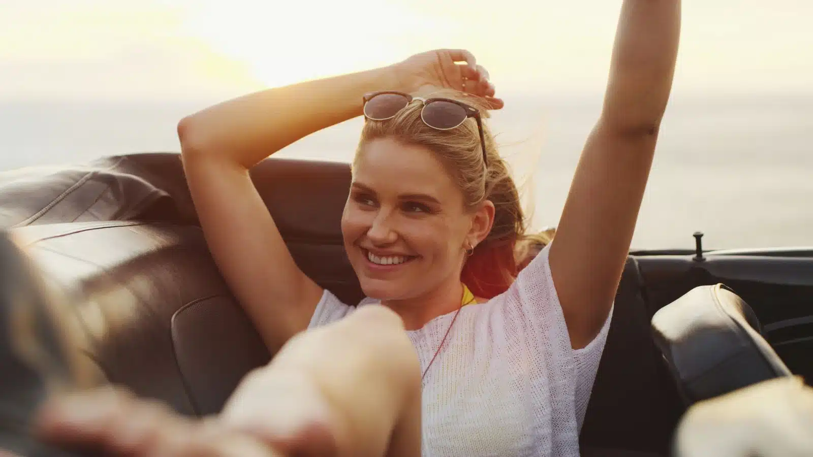 A woman relaxes in the back seat of a car. She looks happy and refreshed.