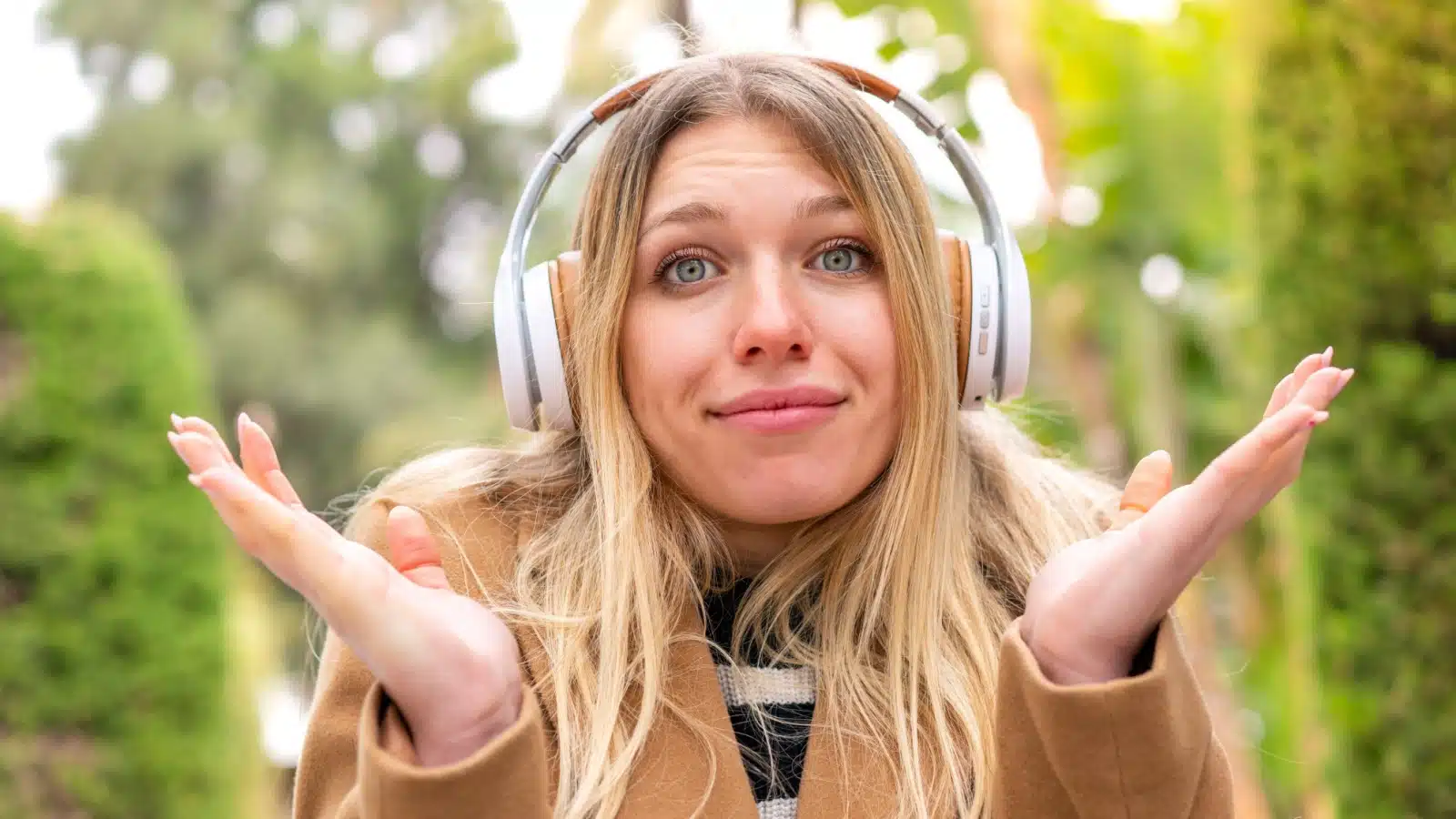 A woman wearing headphones with her hands up in an unsure gesture. She's on the fence about having kids.
