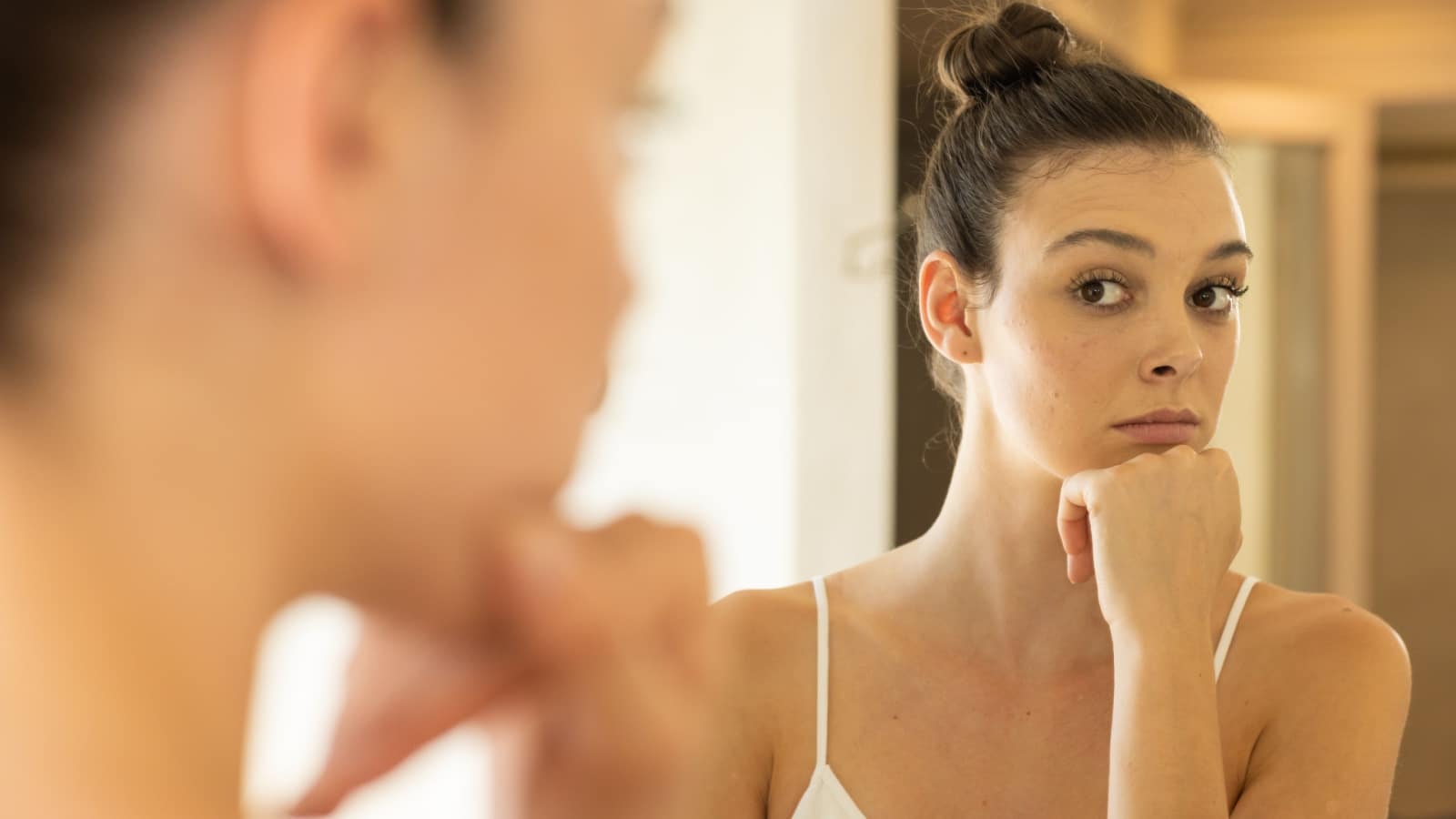 A woman looks in the mirror, judging herself, to represent shadow work.
