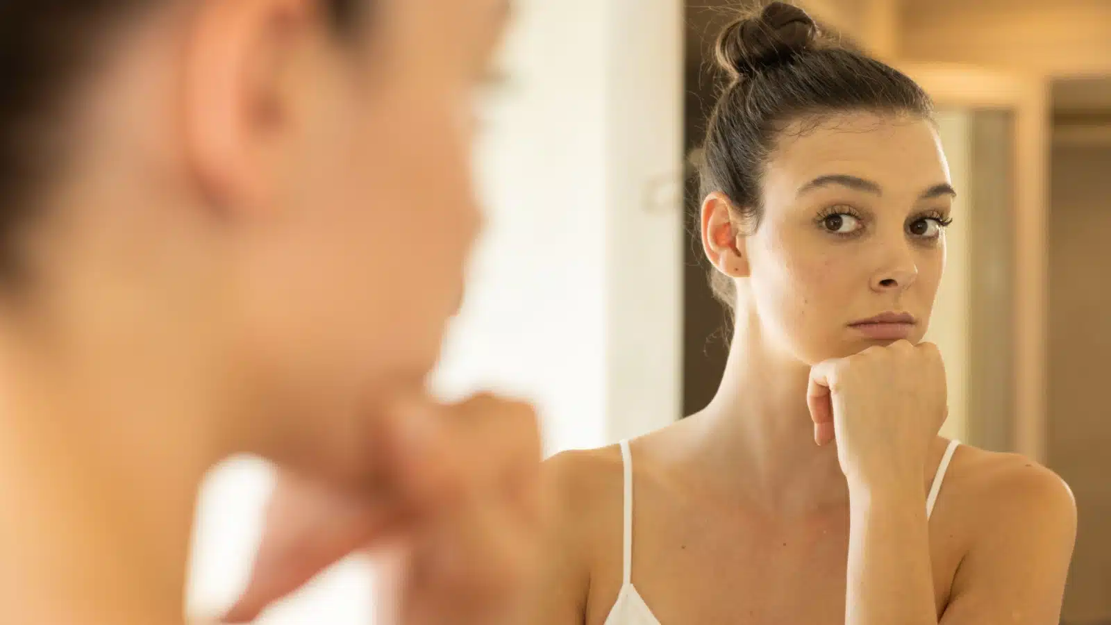 A woman looks in the mirror, judging herself, to represent shadow work.