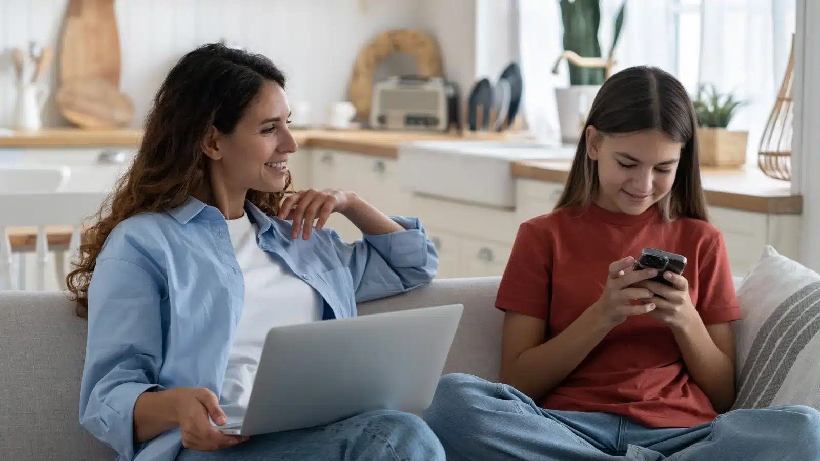 A mom and daughter sit on the couch, using their devices and talking, to represent Discord safety and online safety in general.