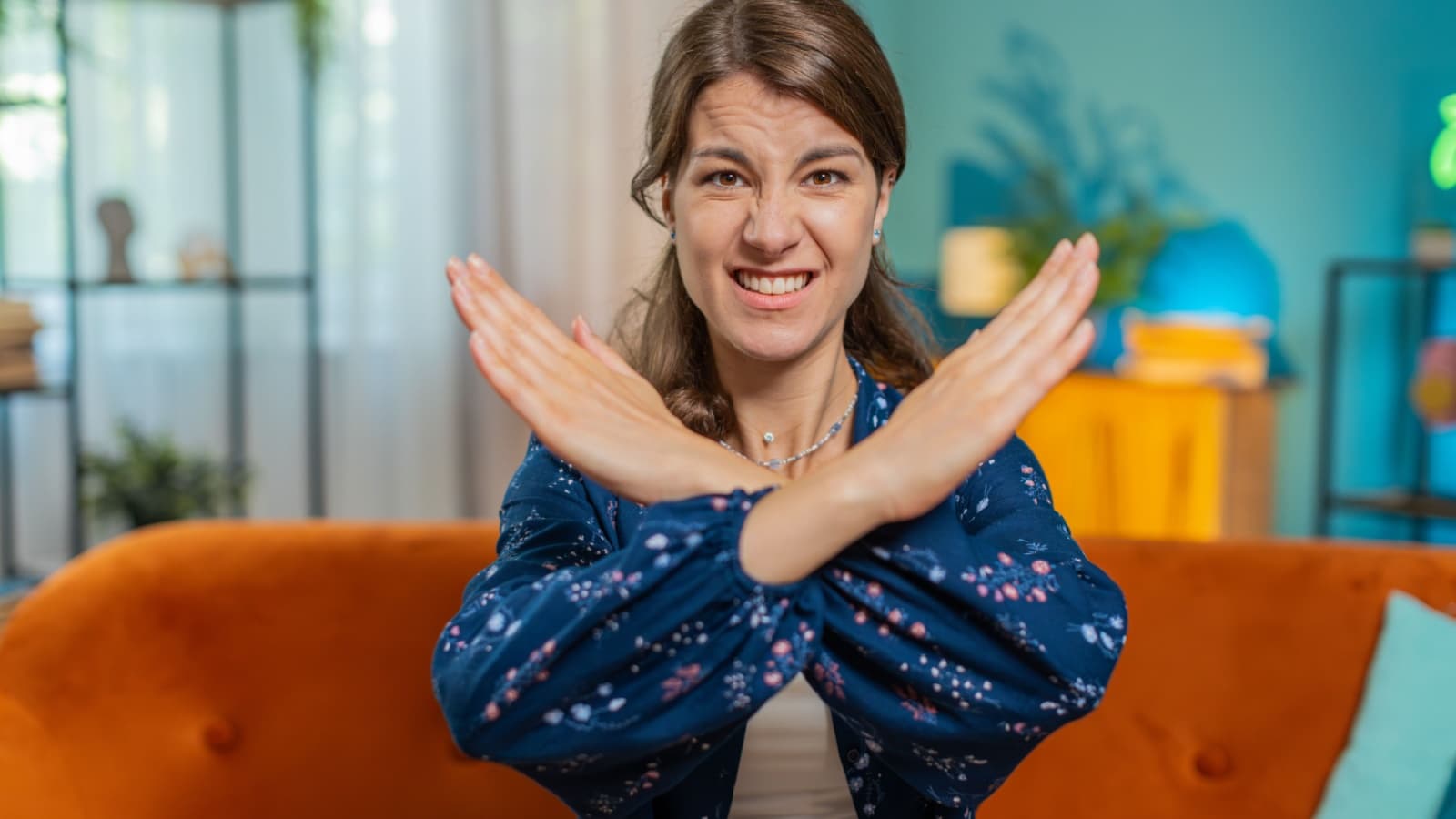 An angry looking woman sits on her couch, making a refusal gesture, to represent the anti-bucket list of things we will never do (again!).