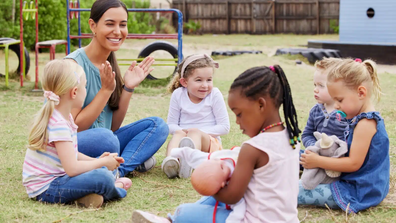 A teacher at a daycare center leading a group of children in an outside play activity.