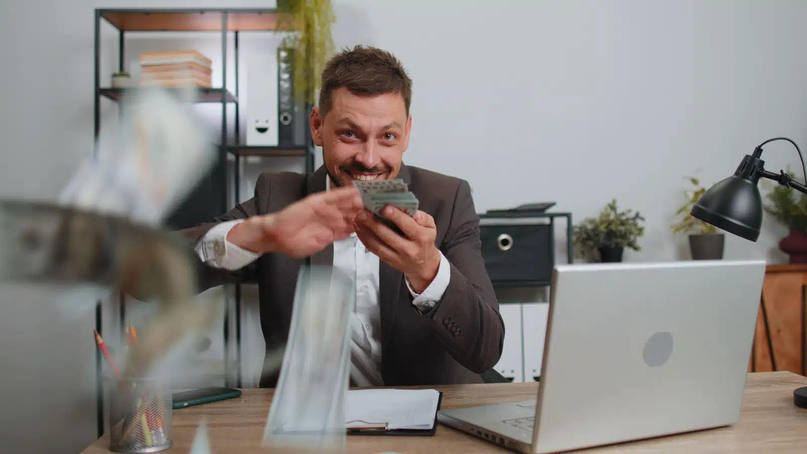 A business man cheerfully throwing money around to represent how companies waste money.