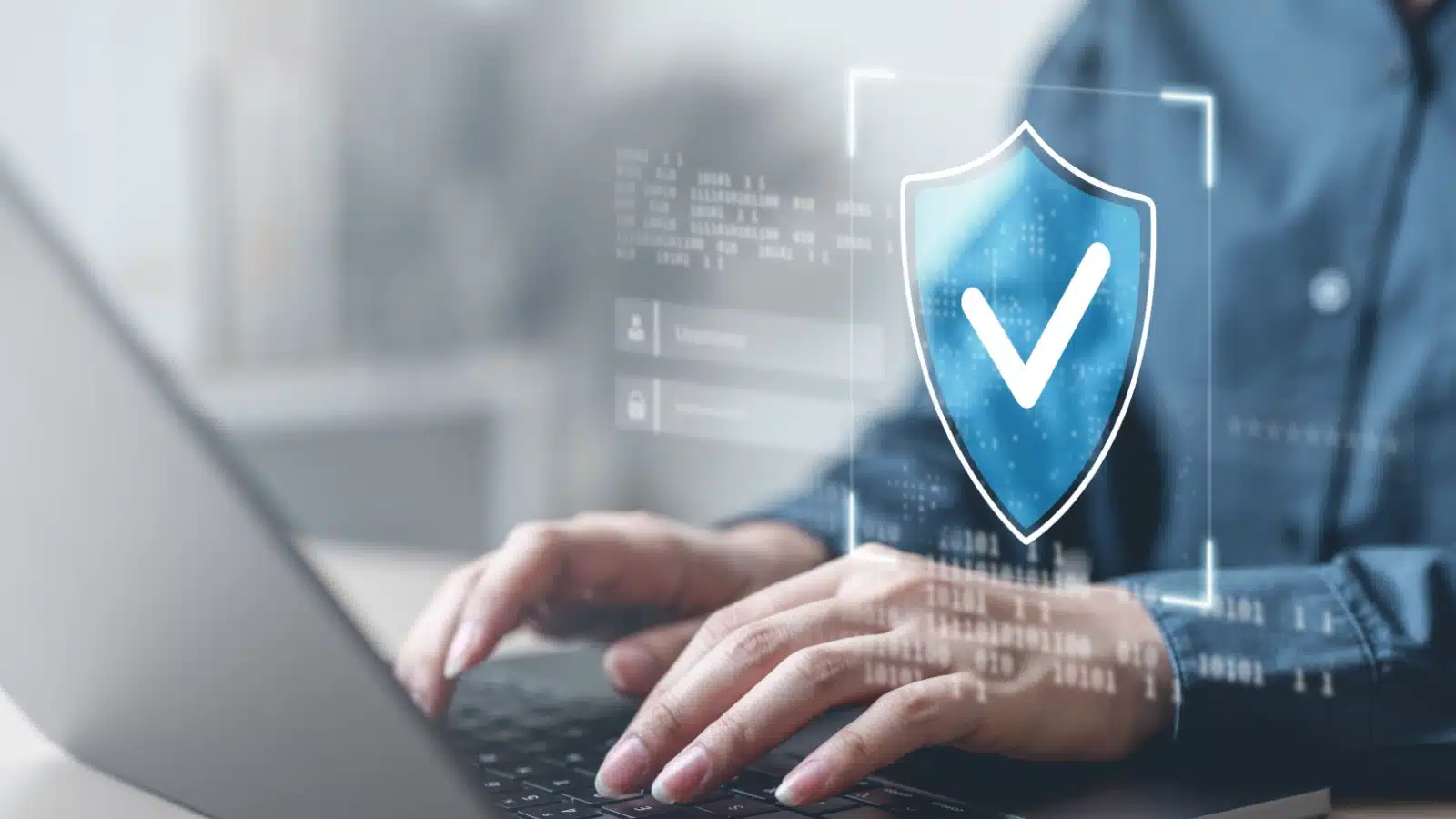Person using a laptop with an image of a security checkmark overlayed to represent cyber security.