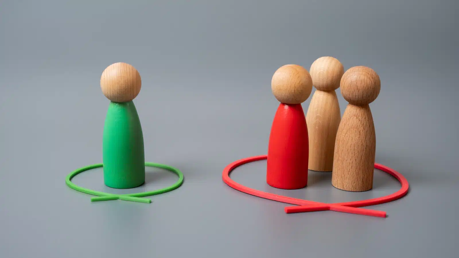 Four wooden models highlight how people who are different are often excluded from social events. A green model stands alone in a green circle, while three reddish models stand together in a red circle.