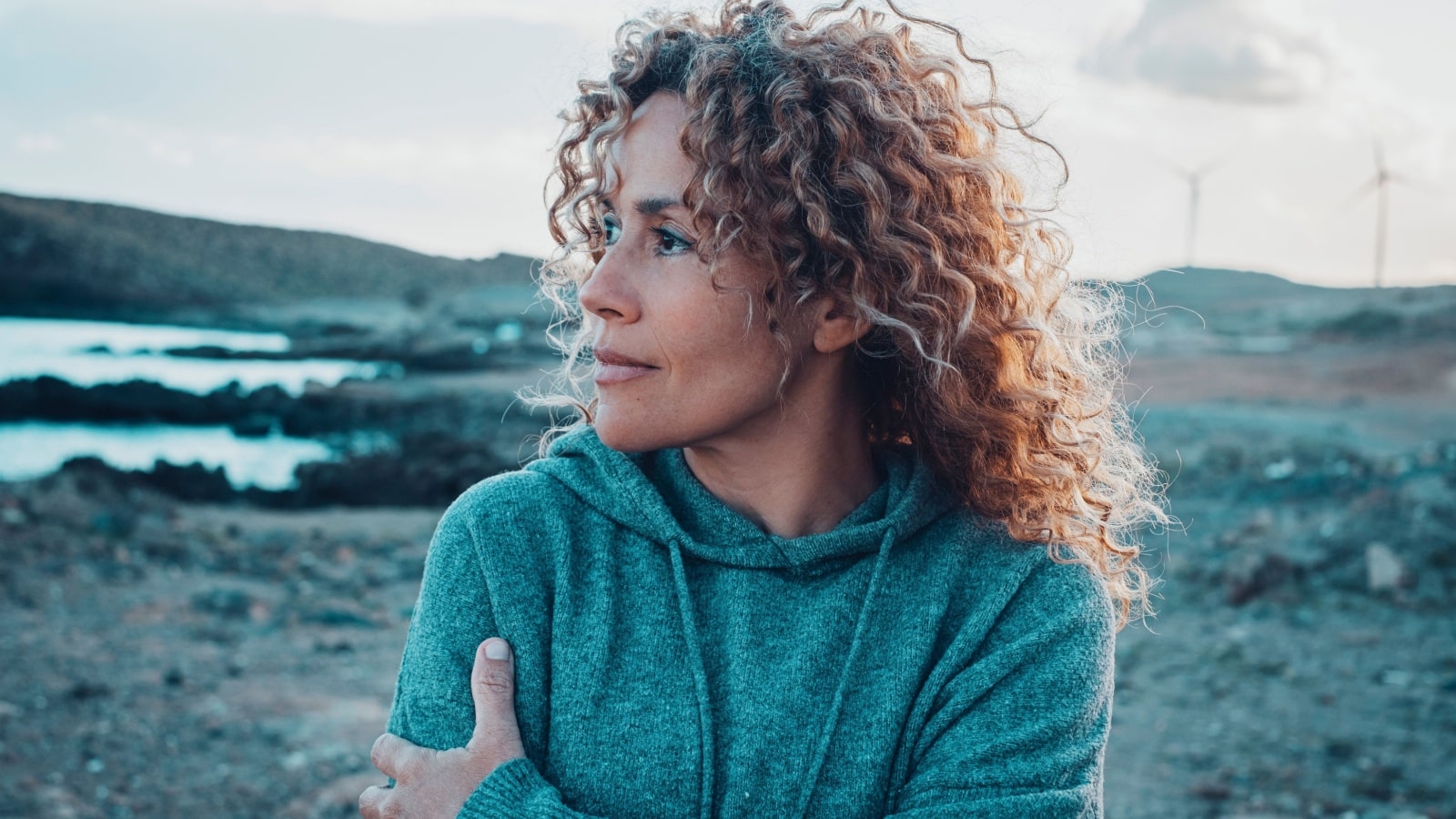 A pensive looking woman stands outside, hugging herself, as if she's experiencing existential dread.