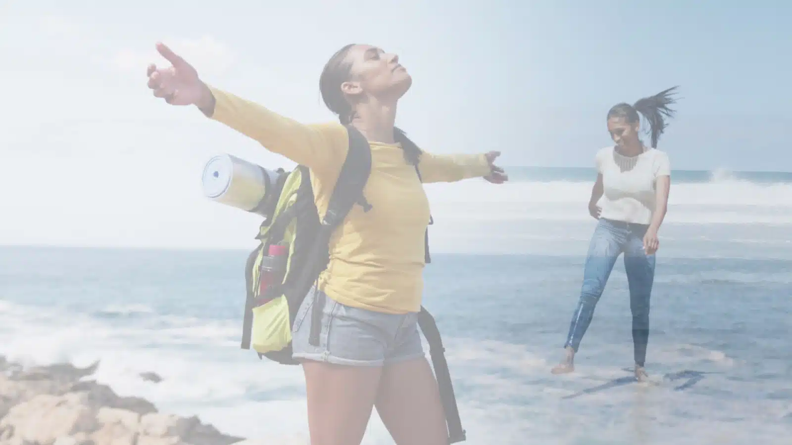 Two free spirited people at the beach highlight that all free spirits are different. One has her arms spread out enjoying the air on her face, while the other plays in the water.