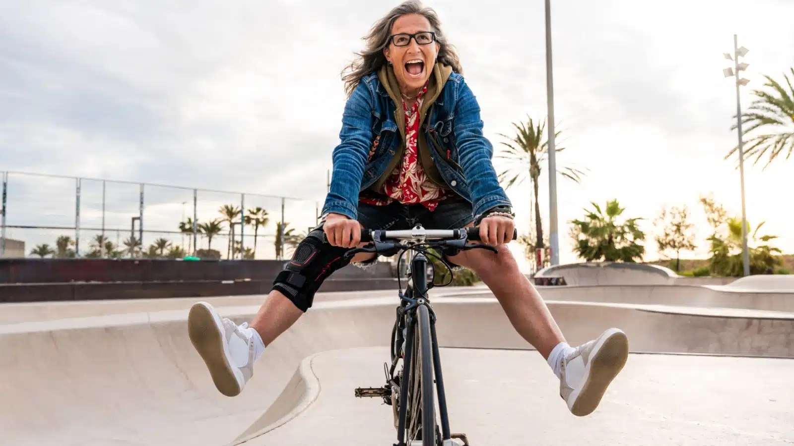 A free spirited older woman rides a bike at skate park.