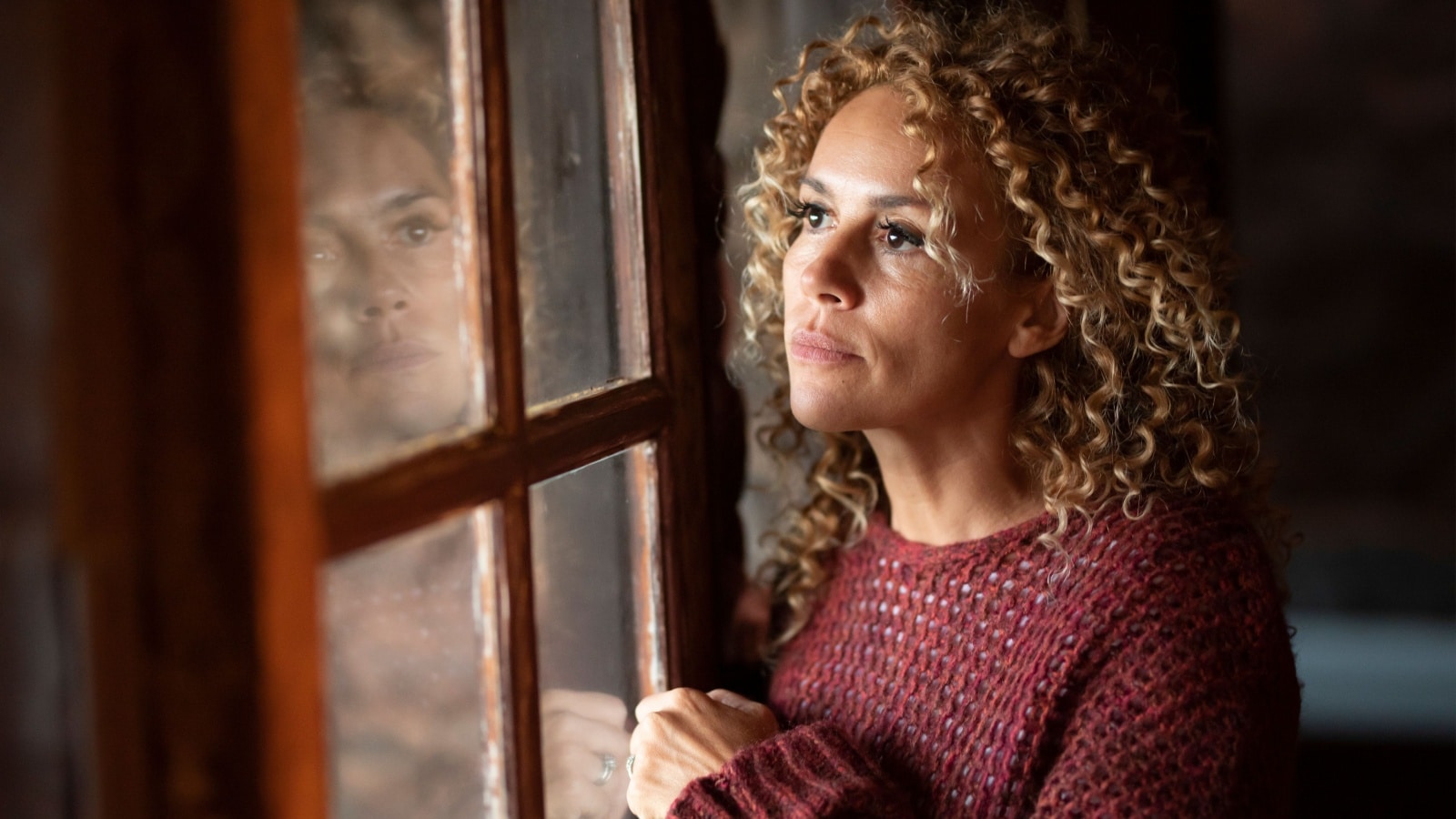A sad woman looks out the window, reflecting, to represent hard life lessons.