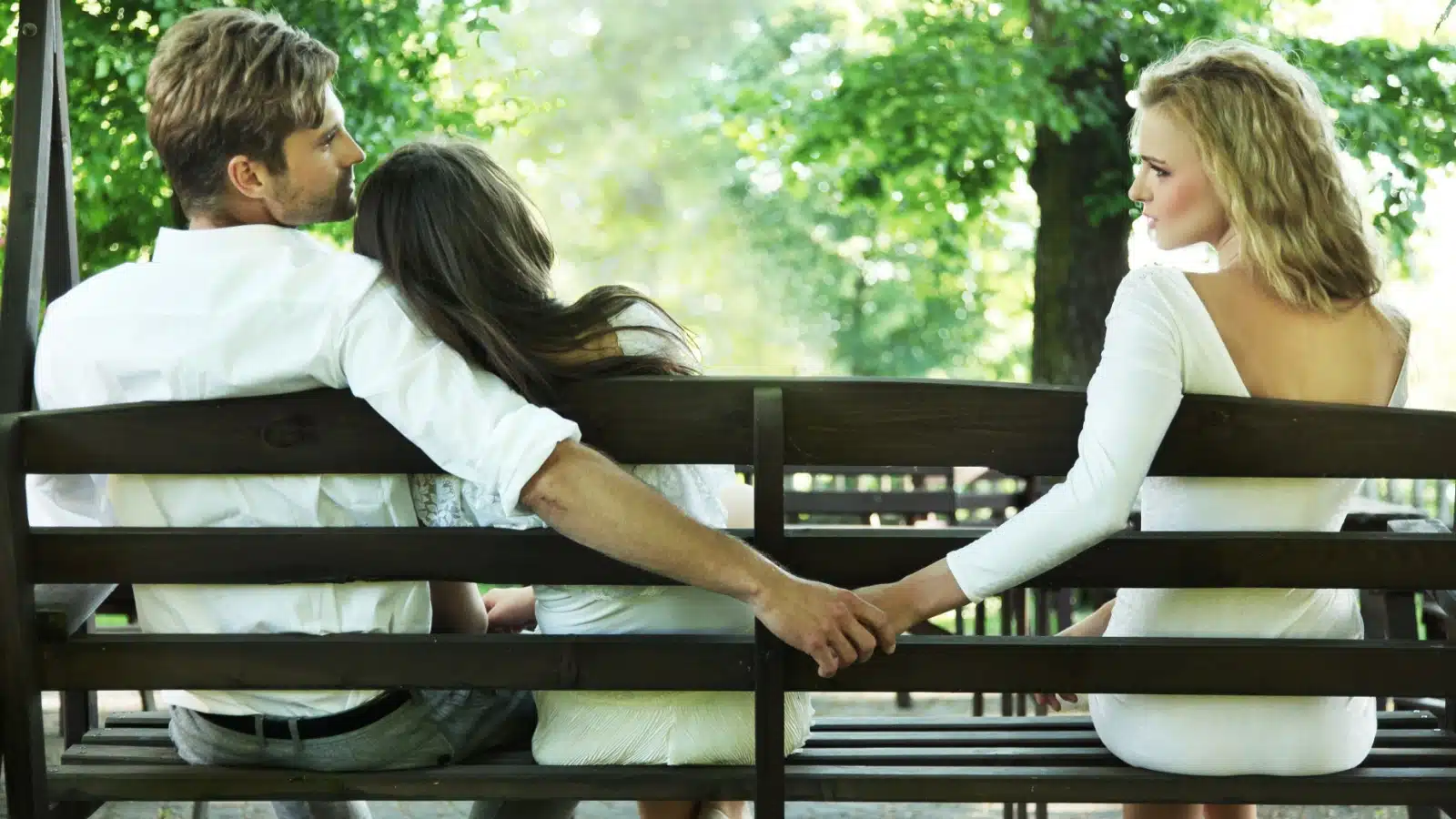 A couple snuggles on a park bench, while the cheating man slyly holds hands with an affair partner.
