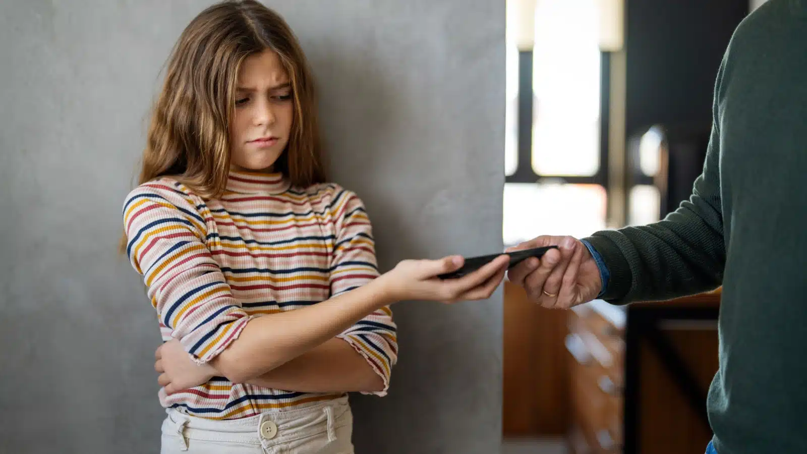 A young girl begrudgingly hands her cellphone to her day, who is limiting her screentime. 