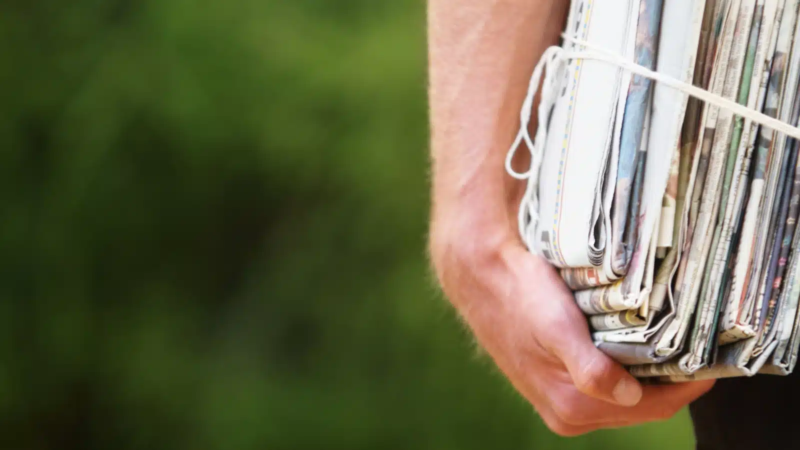 Close up of a man holding a stack of newspapers.