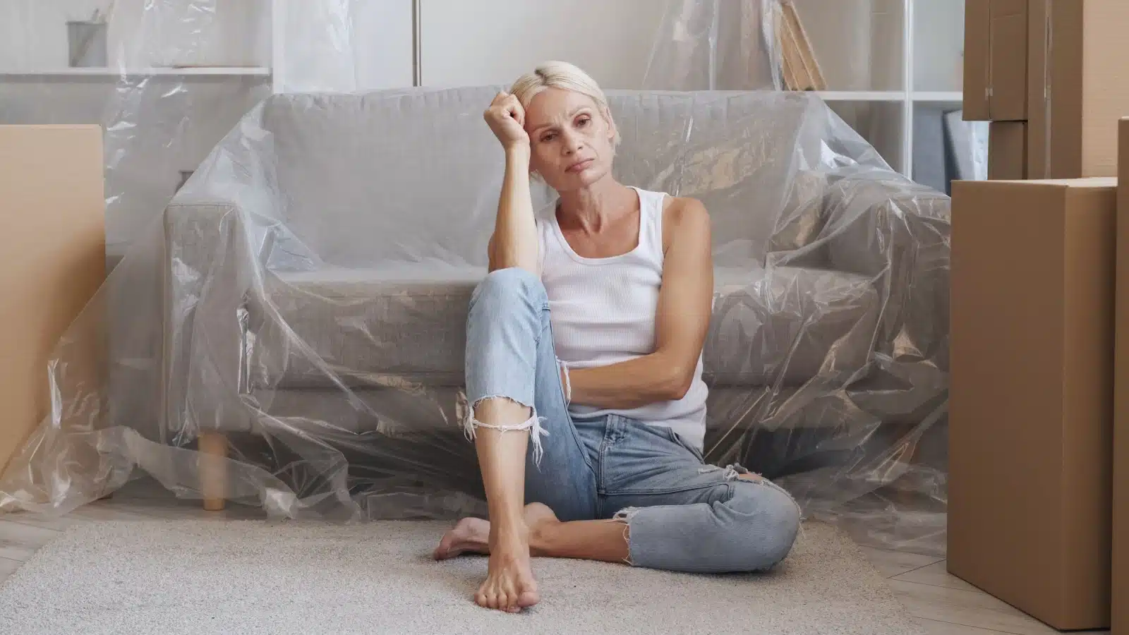 A sad woman sits in her home that's packed up for moving.