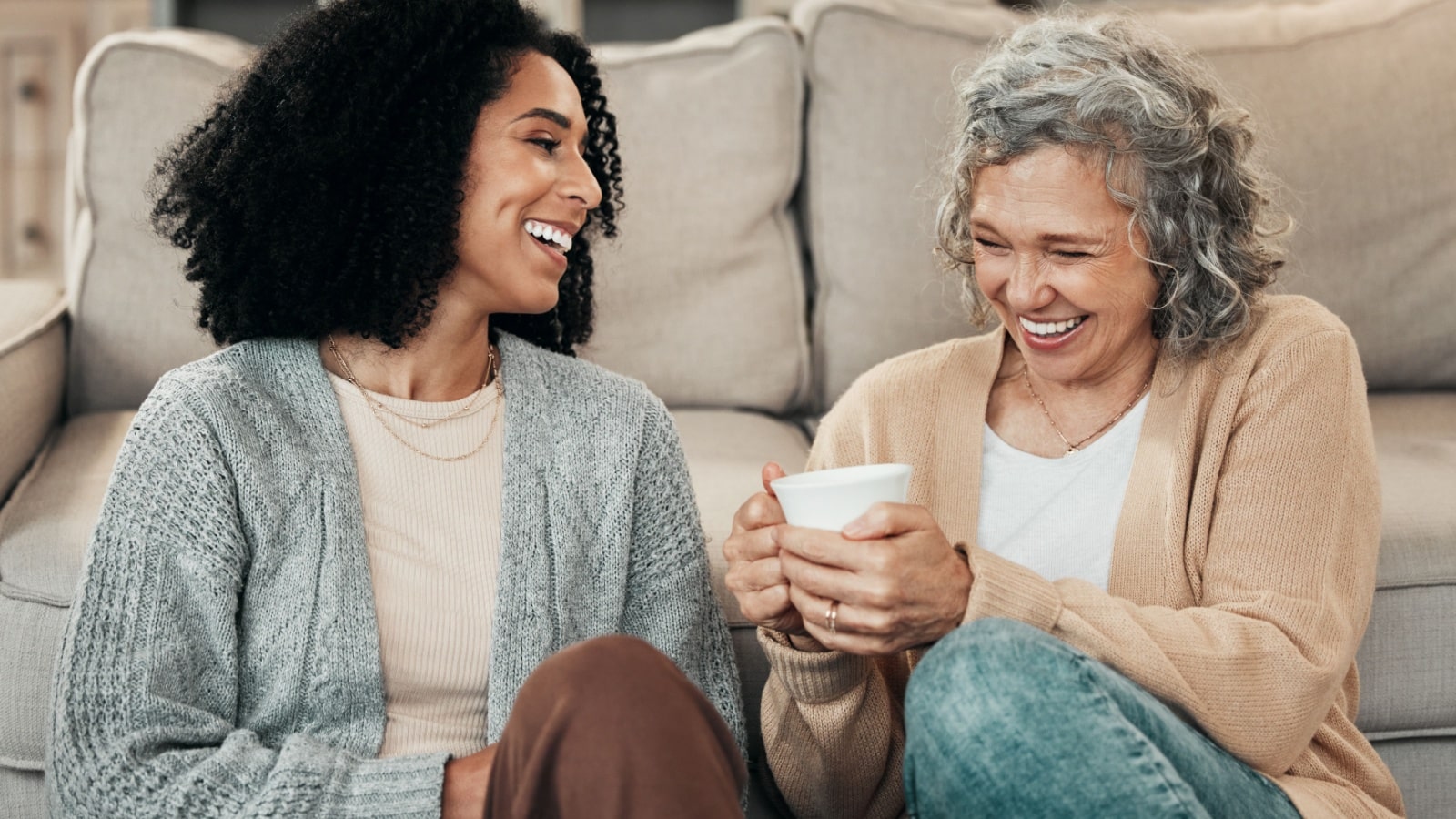 A senior mother with her adult daughter, sitting on the floor chatting.