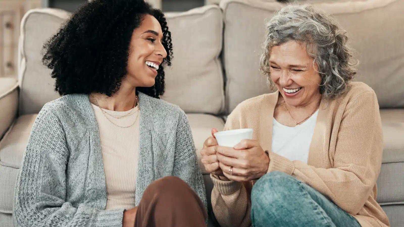 A senior mother with her adult daughter, sitting on the floor chatting.