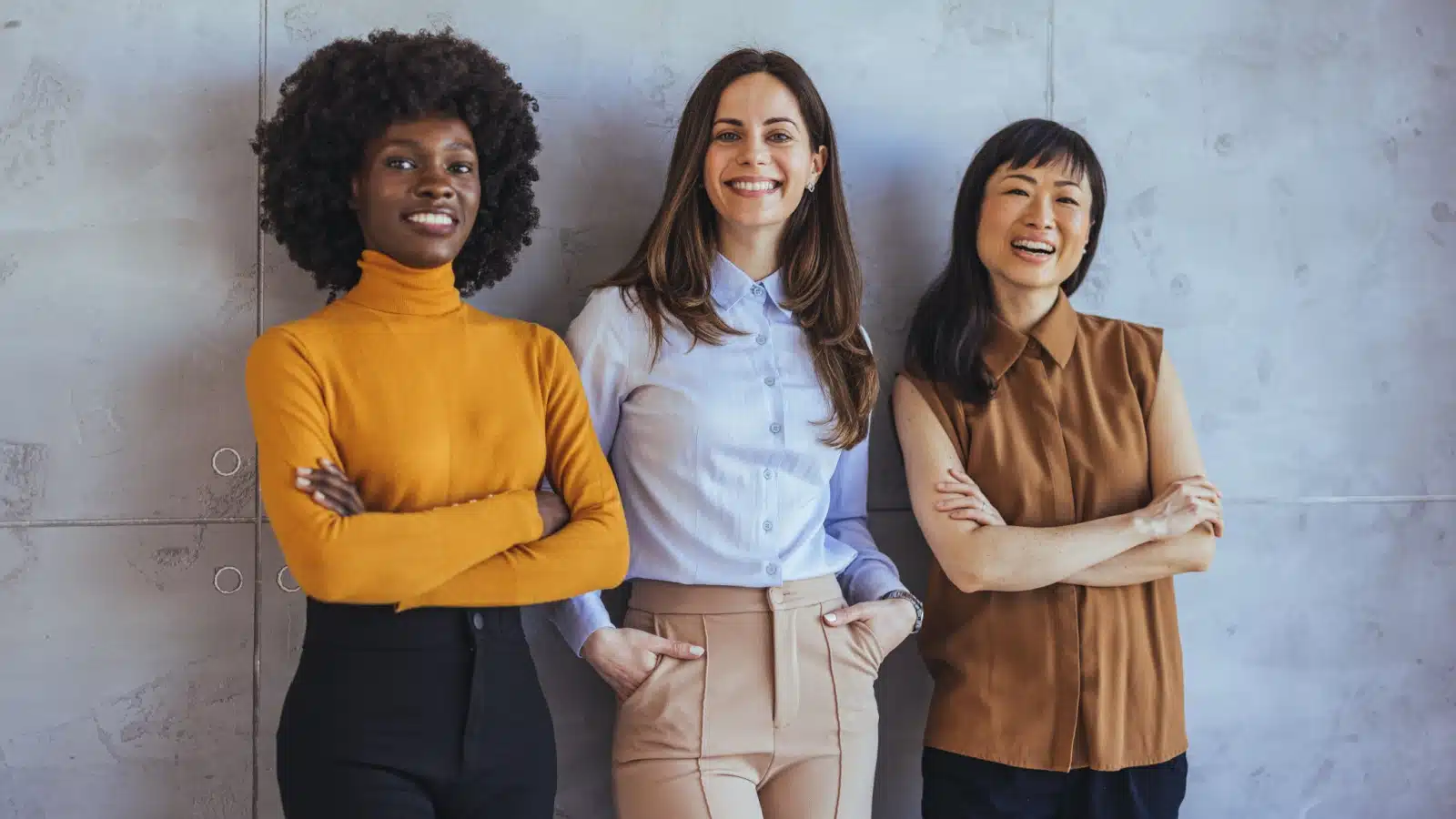Three well dressed women stand together, smiling. 