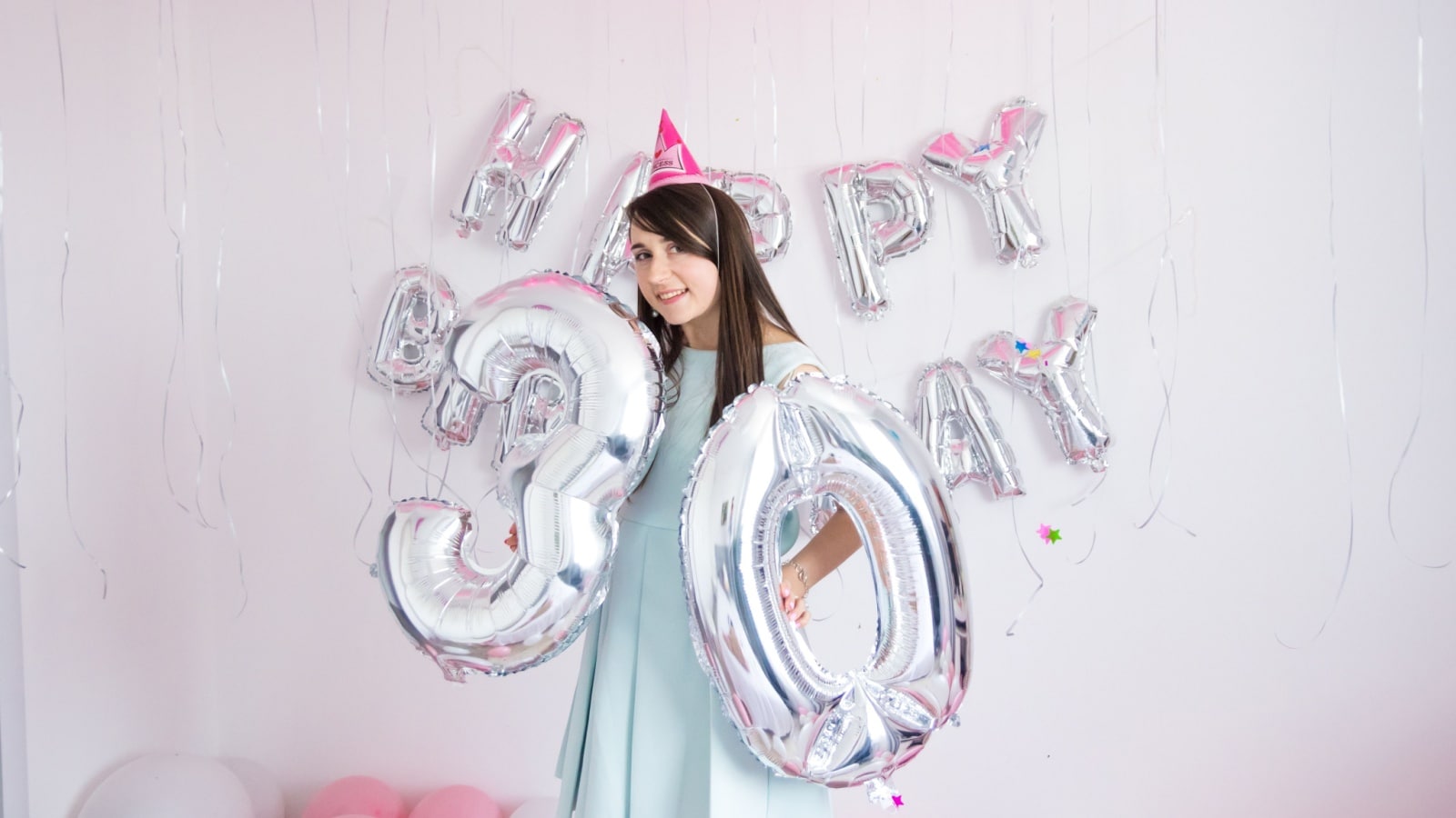 A woman celebrates her 30th birthday by holding up balloons spelling out 30.