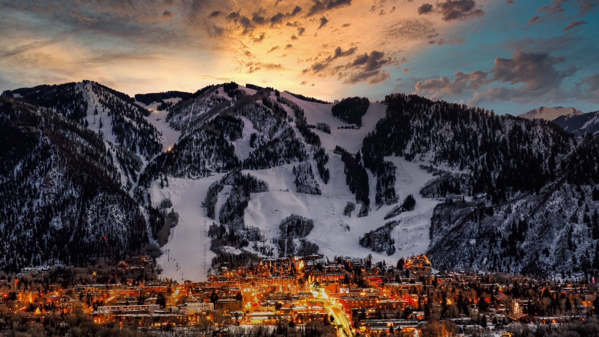 aerial view of Aspen light up in front of a mountain as the sun sets behind the mountain