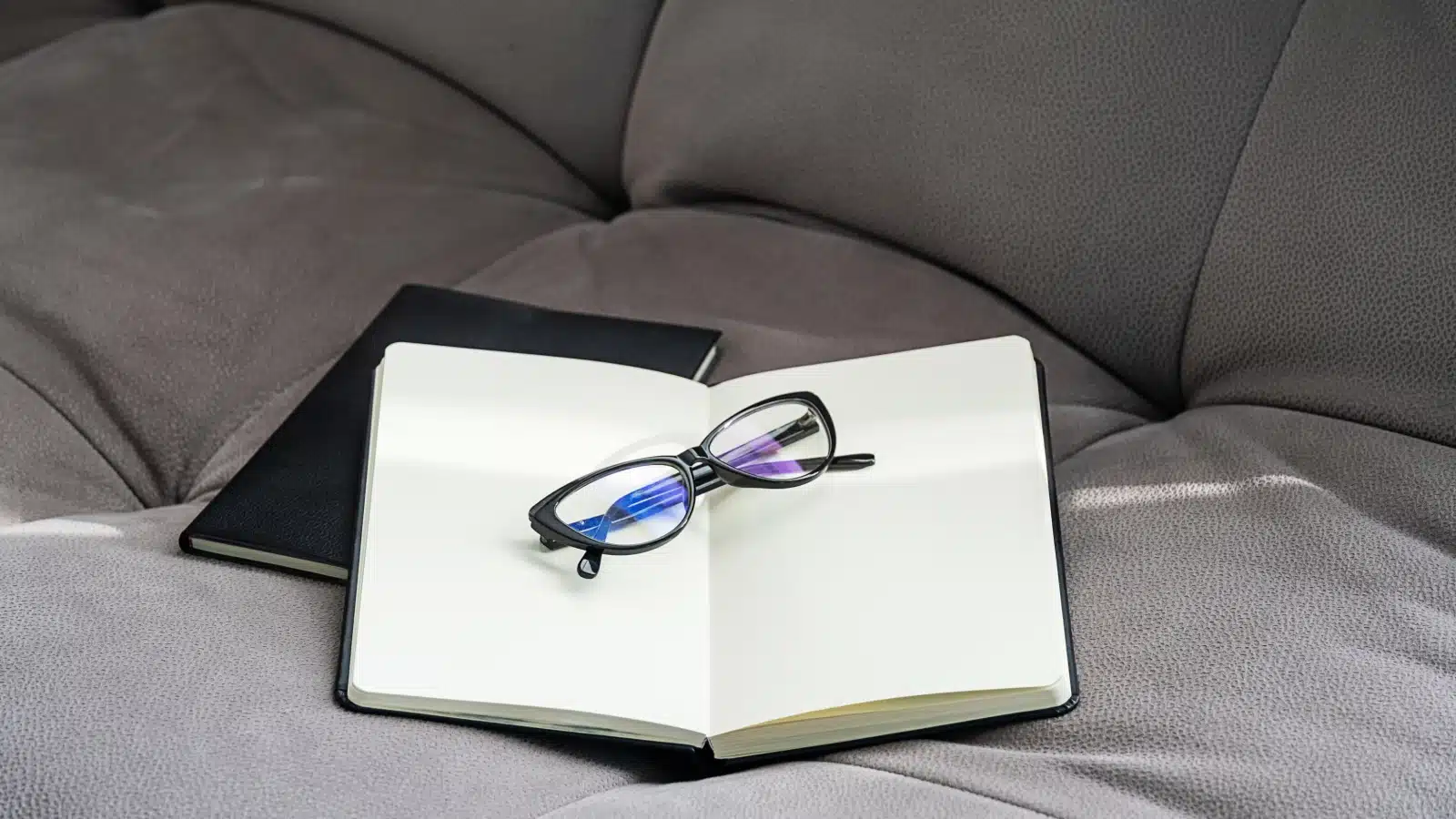An open blank page journal resting on a couch with sunglasses laying across the open pages.