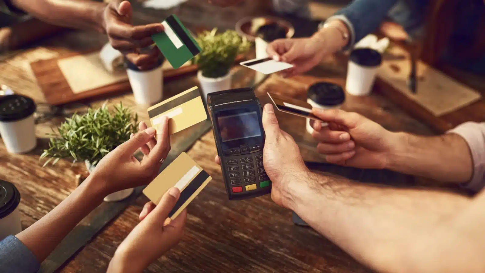 A group of friends at a restaurant. All of them are holding their credit cards out toward the payment machine to pay their fair share of the bill.
