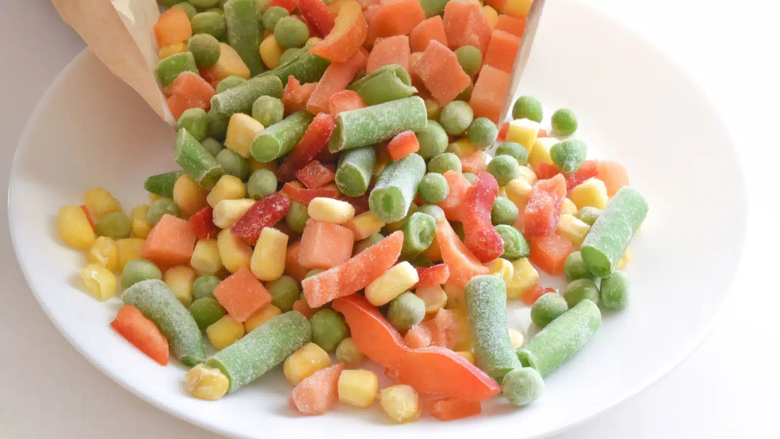 Pouring a bag of frozen vegetables (peas, carrots, corn, and green beans) into a bowl.