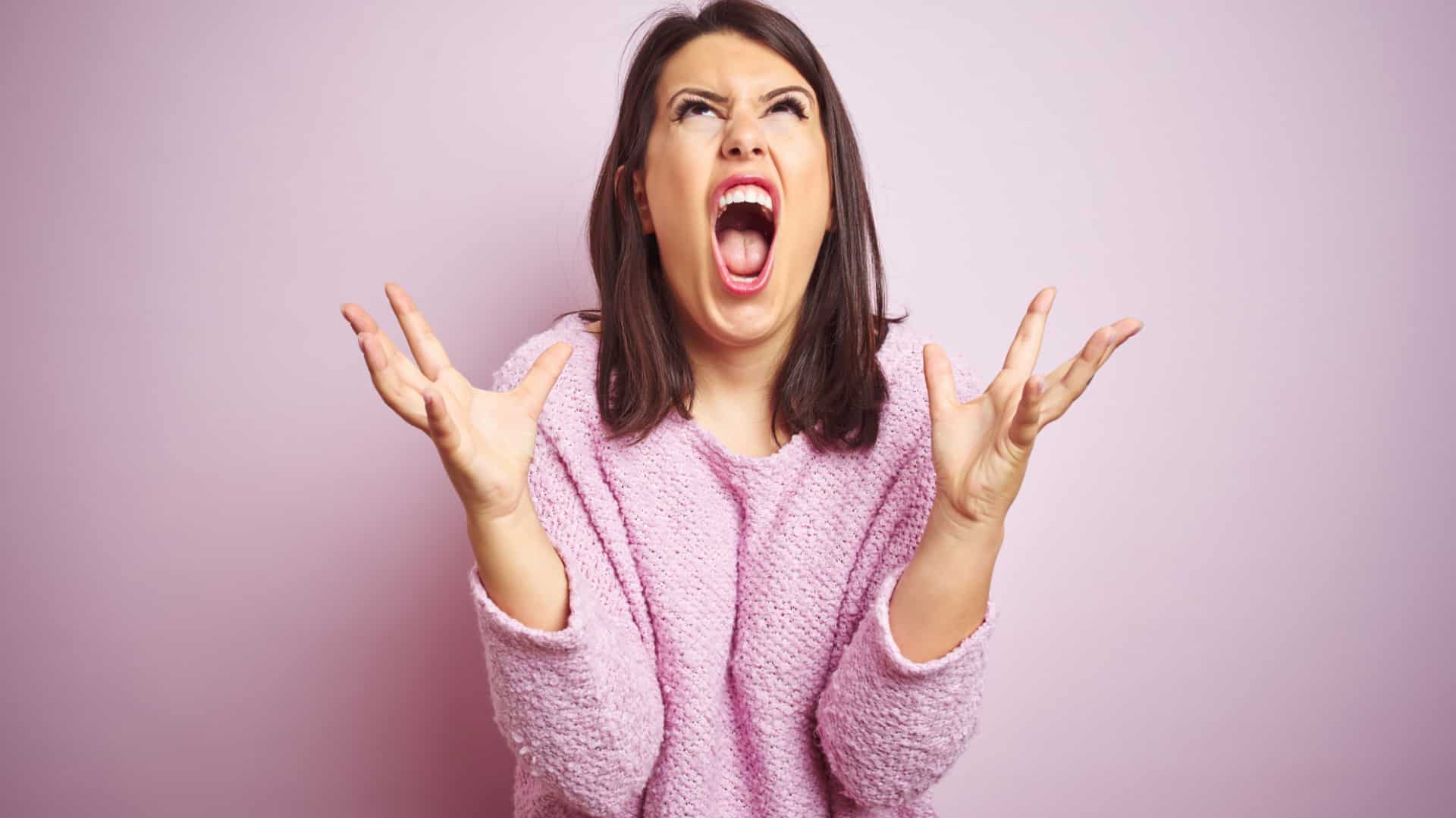 frustrated woman yelling up on a pink background