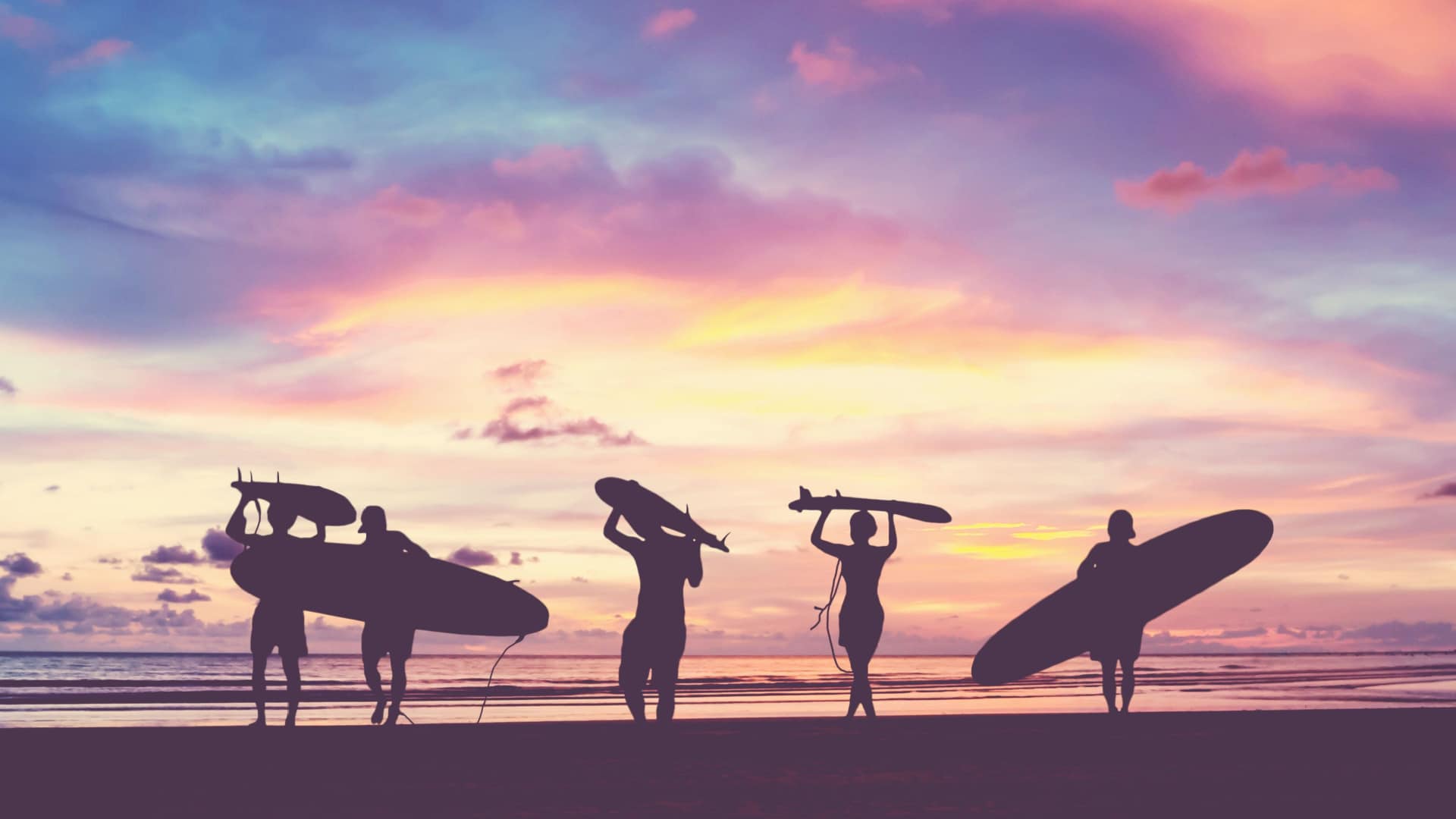Silhouettes of people on the beach holding surfboards