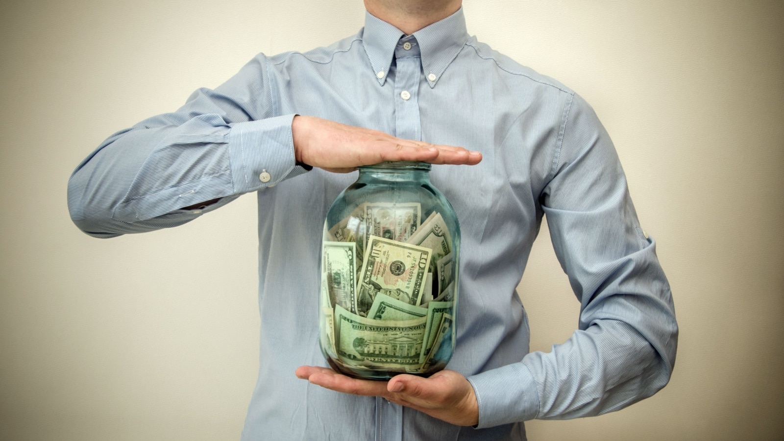 Man holding a jar of money to represent the idea that money is everything.
