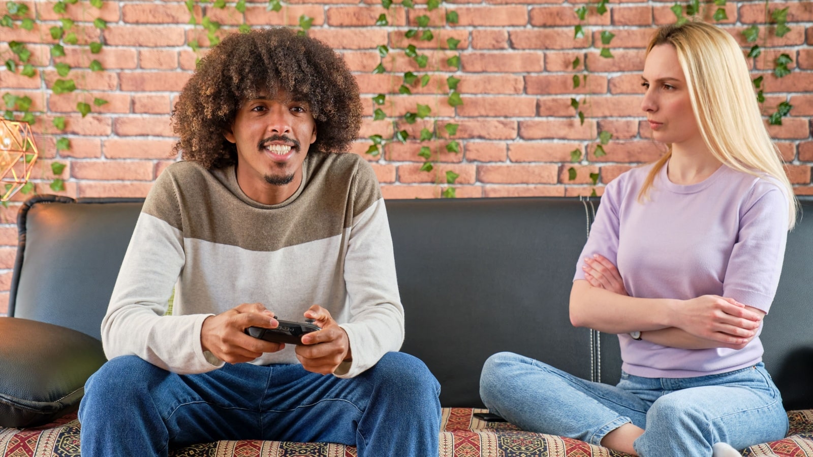 A man happily plays a video game, oblivious to his partner glaring at him, to represent red flag hobbies.