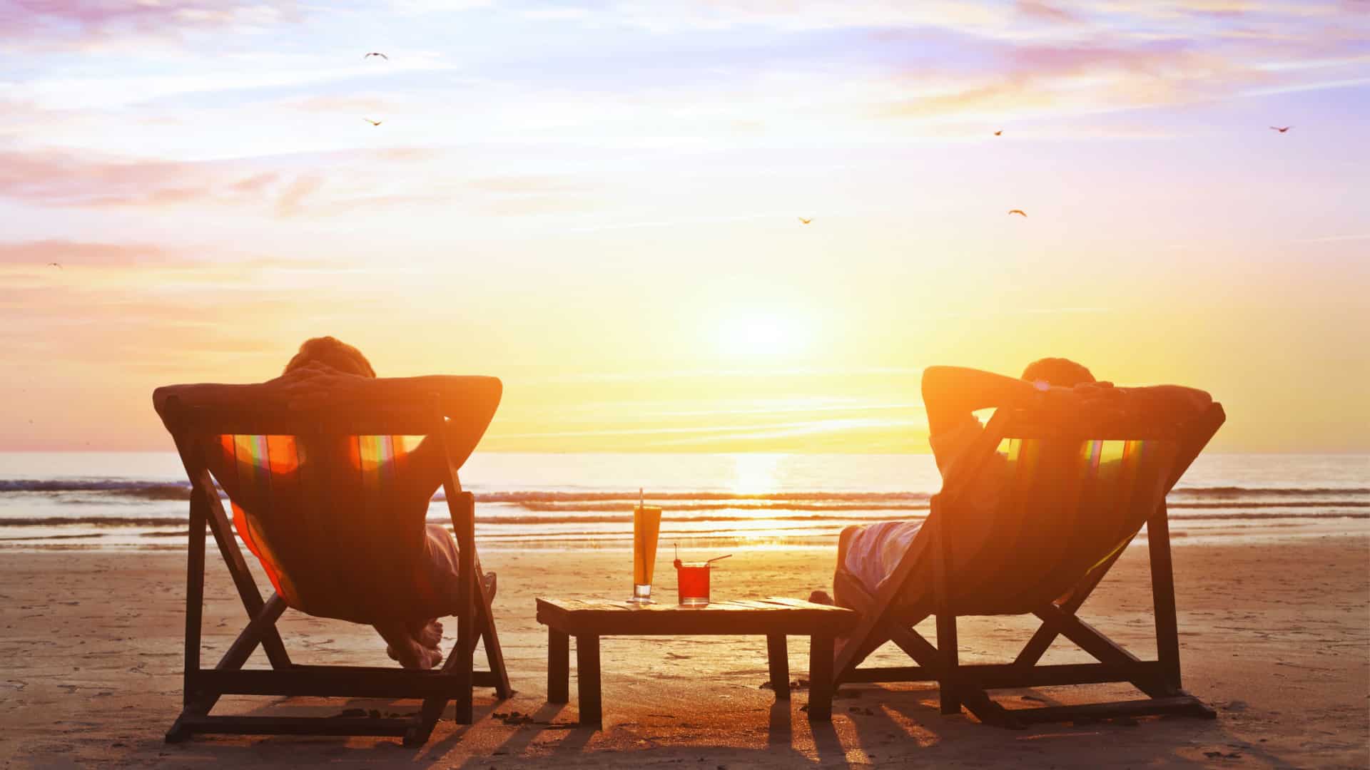 couple relaxing on beach lounge chairs enjoying a sunset on the beach