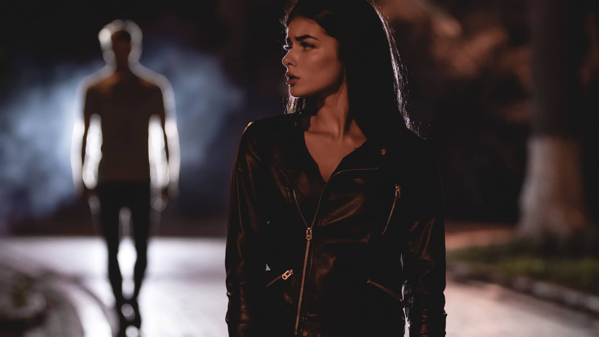 woman walking at night being followed by a creepy man to represent street smarts