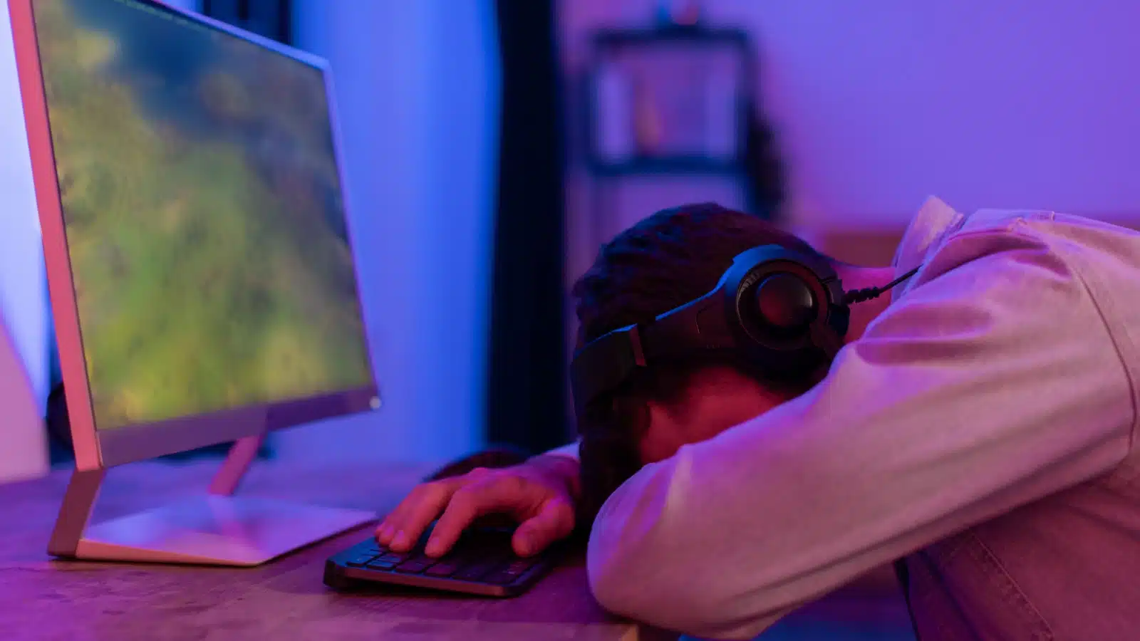A tired man falls asleep at his computer while playing a video game.