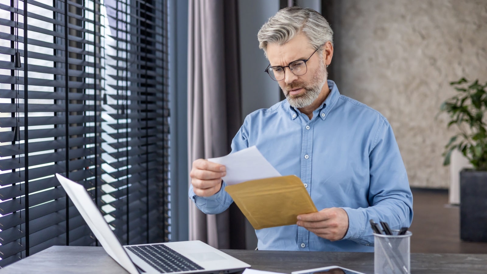 An unhappy looking worker opens a piece of mail at his desk.