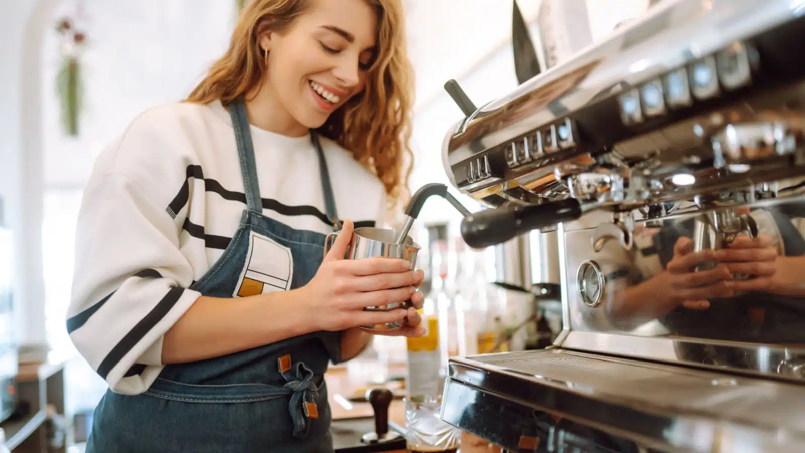 A joyful woman uses an espresso machine to make a coffee drink.