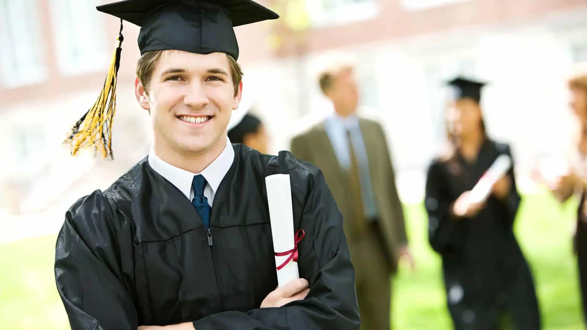 smiling man wearing college graduation robes and holding a diploma