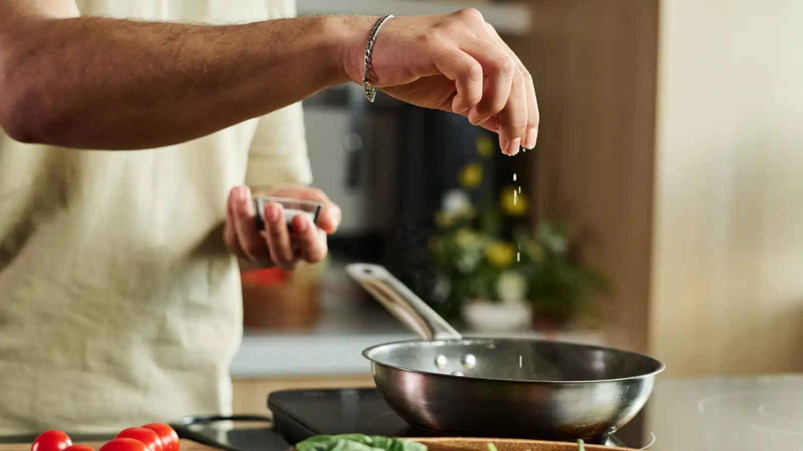 A man slowly adds a pinch of salt to the pan while cooking.