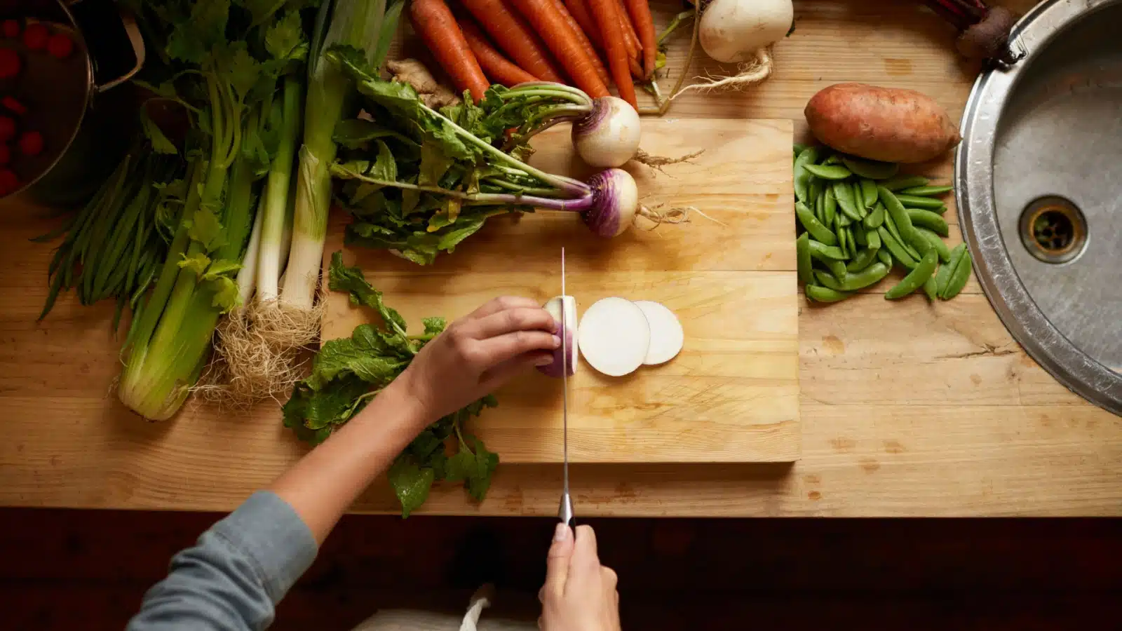 Top view of hands cutting fresh vegetables using a cutting board.
