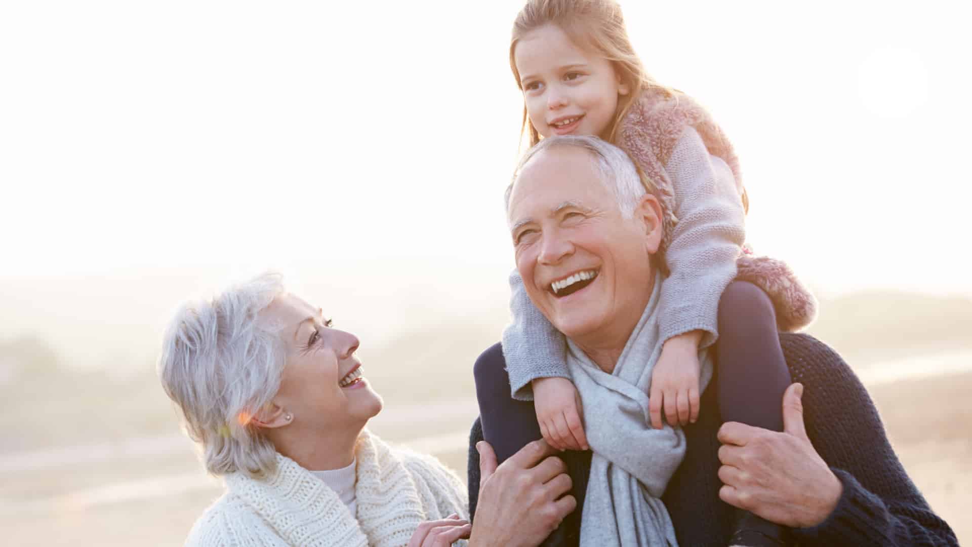 grandaughter riding on grandpa's shoulders with grandma smilling at them.