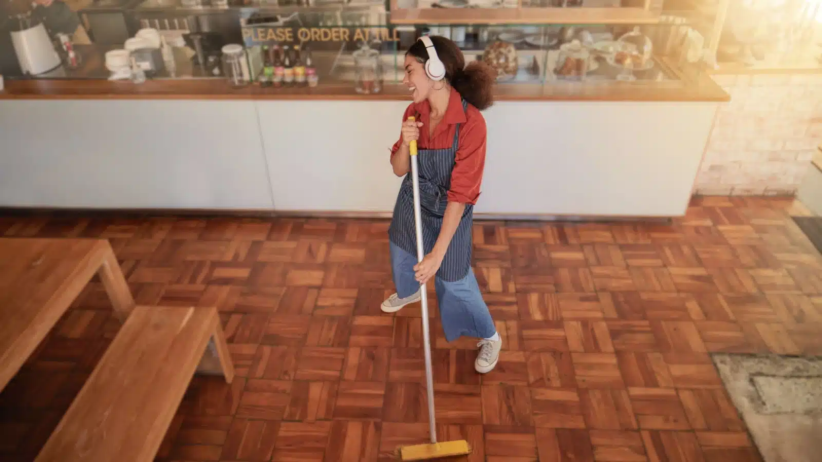 A happy woman sings and dances while sweeping the floor at her easy job.