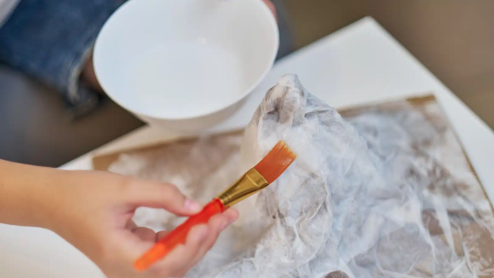 A woman paints a papier mache project with papier mache paste.