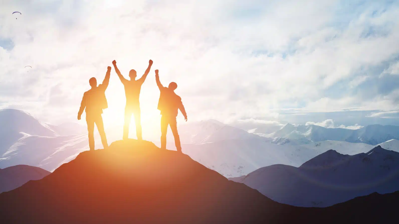 Silhouettes of three businessmen celebrating atop a mountain to ask what is success?