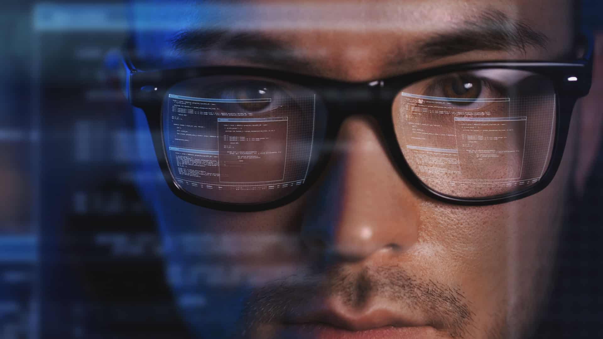 Man wearing glasses. You can see the reflection of the computer screen on his face and in his glasses and he look serious like he's a hacker.