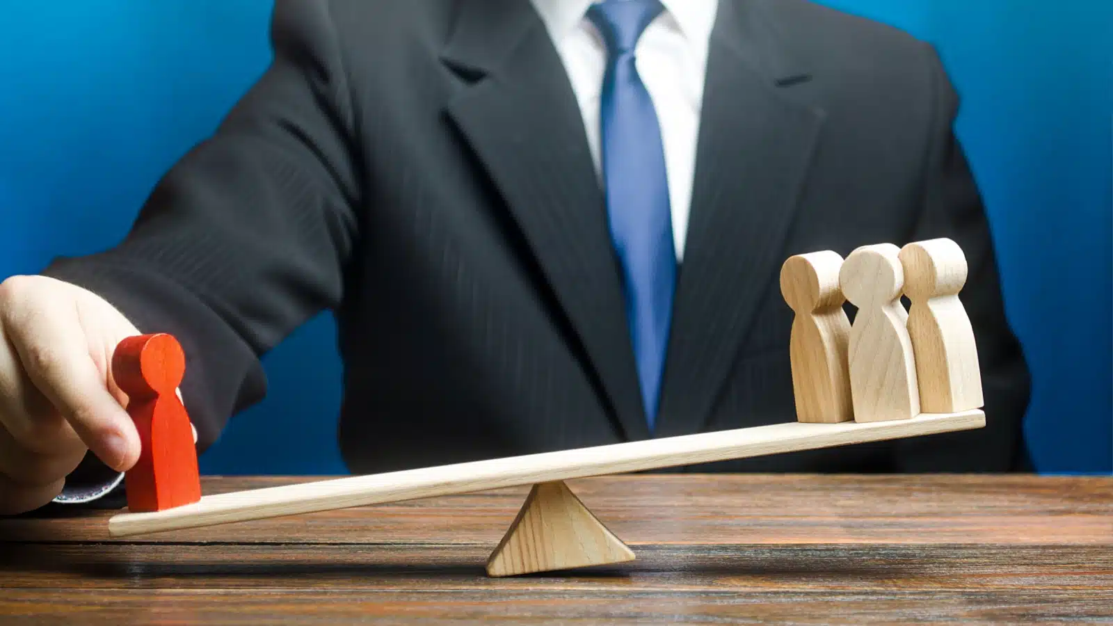 Concept photo representing nepotism at a work. A businessman pushes the scale down on the red wooden figure that represents his friend, giving the red one more weight than the rest of his employees.