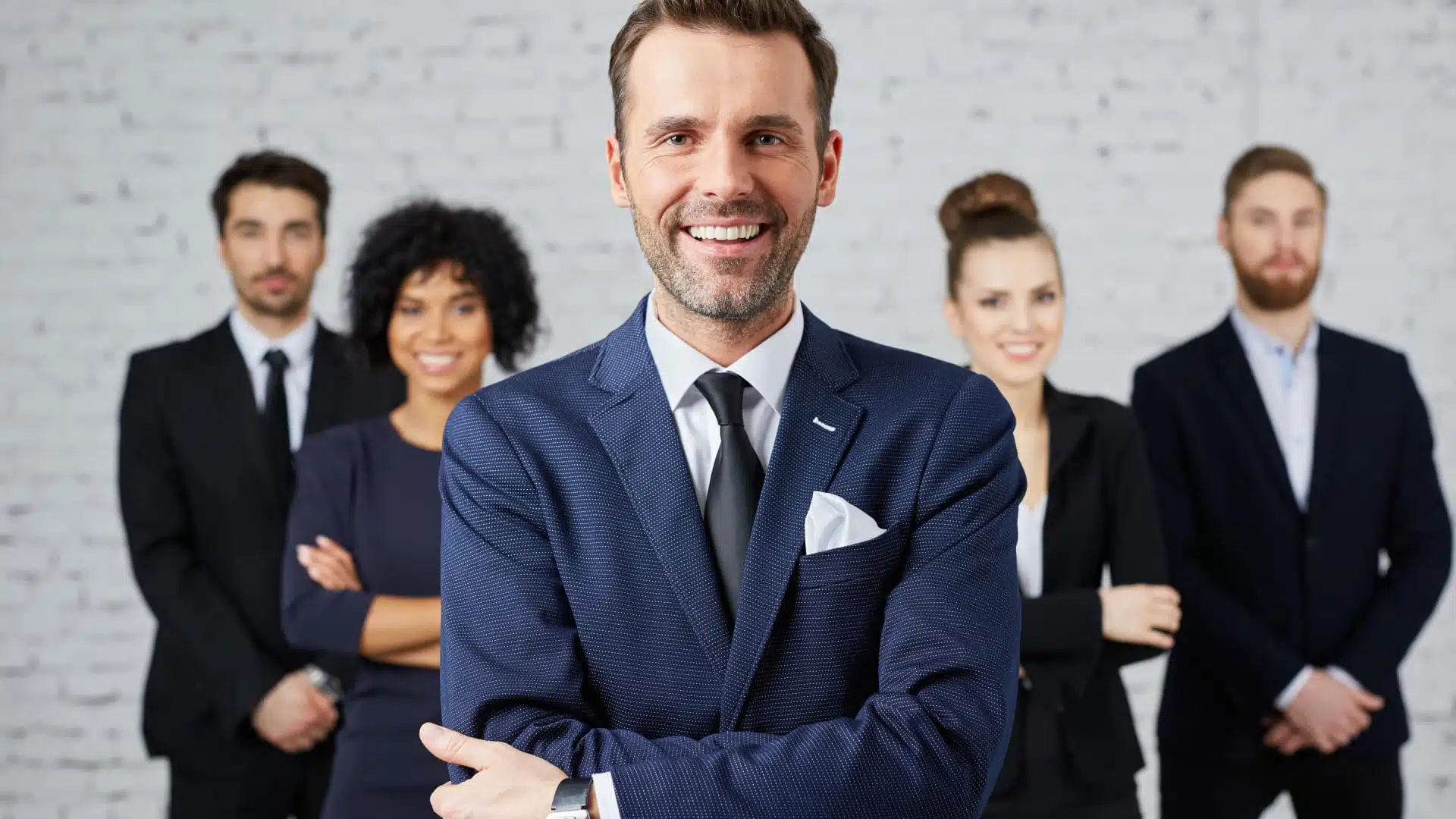 A smiling business man stands in front of his team.