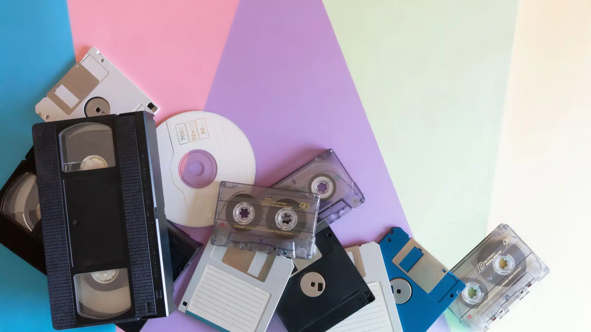 An assortment of 90s electronics to include VHS tapes, cds, floppy disks, and cassette tapes.
